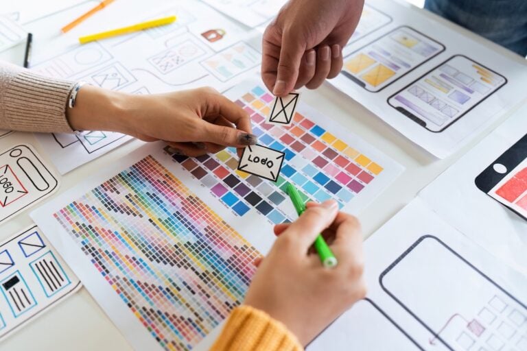Two people brainstorming about mobile app interface wireframe design on desk at office.
