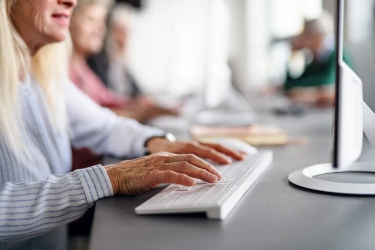 Woman with wrinkled hands typing on a white keyboard.