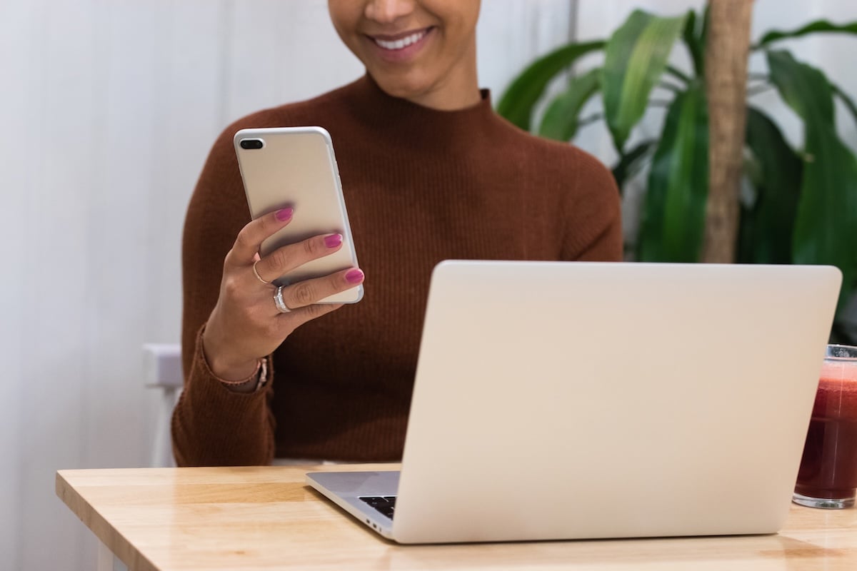Business woman looking at cell phone while laptop is open on table.