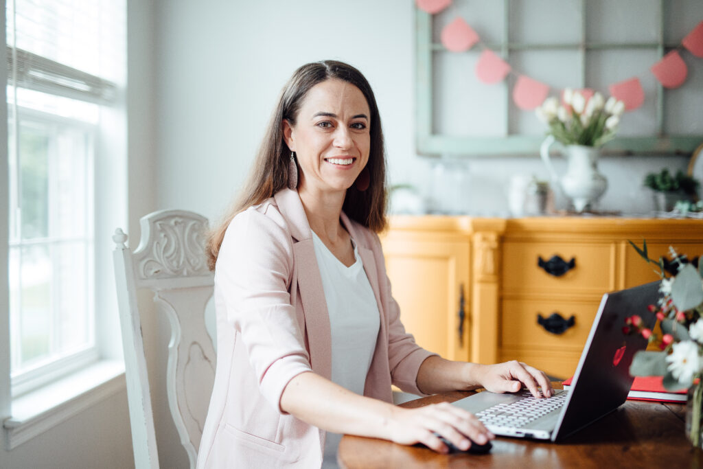Smiling woman is sitting at table with a laptop.